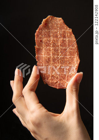 Pork natural jerks in hand on a black background.	 Pork natural jerks in hand on a black background.	 122142908