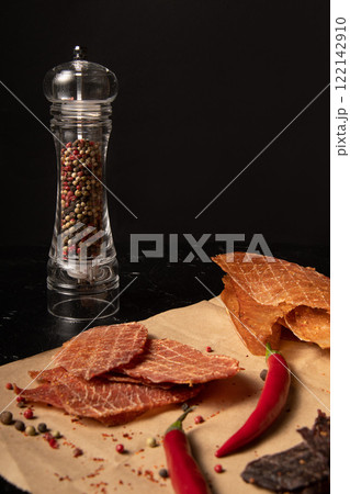 Jerky on craft paper and black background with spices. Jerky on craft paper and black background with spices. 122142910