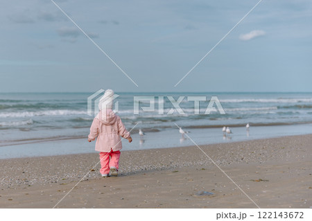 Child girl walking on ocean coastline and watching seagulls. Winter time. Child girl walking on ocean coastline and watching seagulls. Winter time. 122143672