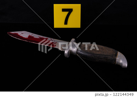 Combat knife in blood next to yellow marker with crime scene number black background 122144349
