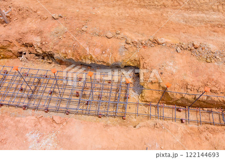 Construction work in progress with rebar grid laid in trench at site, showcasing groundwork for upcoming structure. 122144693
