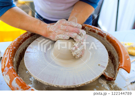 Potter skillfully molds wet clay into vessel on spinning wheel in well lit creative art studio 122144789