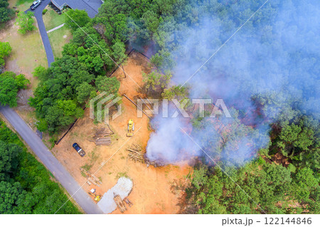Controlled burn creates smoke as land clearing occurs in forested area, surrounded by trees, equipment. 122144846