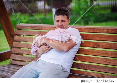 Caring father holding newborn daughter in soft pink blanket, sitting on wooden swing during peaceful backyard moment Caring father holding newborn daughter in soft pink blanket, sitting on wooden swing during peaceful backyard moment 122148133