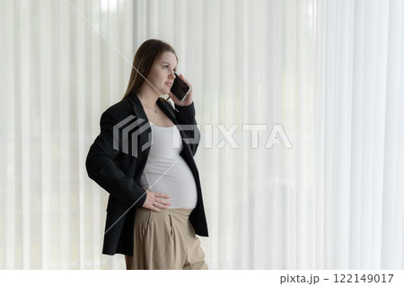 White pregnant woman talking on the phone. Pregnant businesswoman talking on the phone while working. White pregnant woman talking on the phone. Pregnant businesswoman talking on the phone while working. 122149017