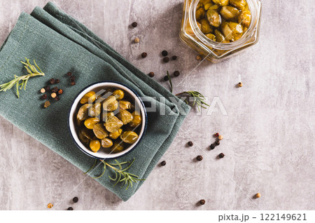 Pickled capers with spices in a bowl and in a jar on the table top view 122149621