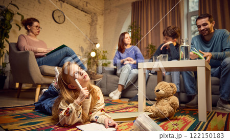 Focus on young girl, child lying on floor and drawing with thoughtful face, while her parents and teen brother talking with psychologist Focus on young girl, child lying on floor and drawing with thoughtful face, while her parents and teen brother talking with psychologist 122150183