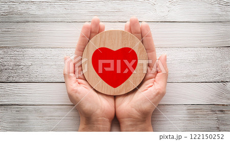 Hands Holding Wooden Heart Symbol of Love and Care on White Rustic Background 122150252