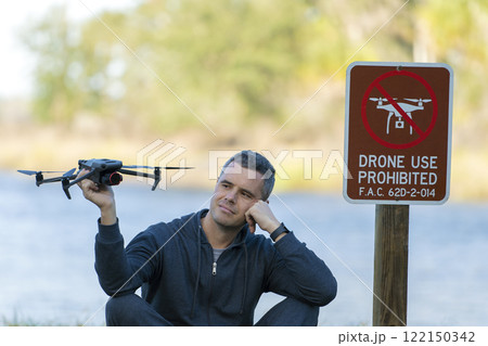 Man is going to fly his quadcopter in no drone area. Operator unlawfully using his UAS in state park near restriction sign Man is going to fly his quadcopter in no drone area. Operator unlawfully using his UAS in state park near restriction sign 122150342