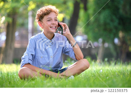 Happy young boy talking on cellphone outdoors in summer park Happy young boy talking on cellphone outdoors in summer park 122150375