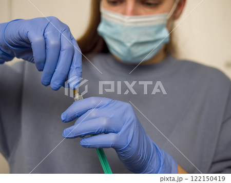 Medical professional in protective gear handling syringe, preparing vaccine injection with sterile medical equipment, demonstrating careful healthcare practices 122150419