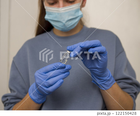Female medical professional in protective gear handling vaccine vial, preparing for immunization process with clinical precision Female medical professional in protective gear handling vaccine vial, preparing for immunization process with clinical precision 122150428
