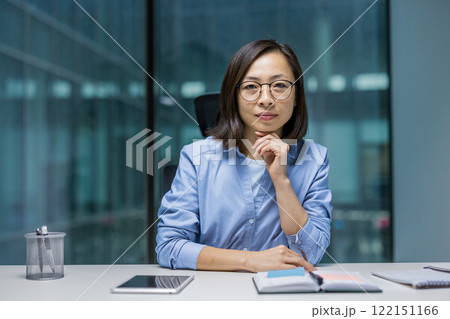 Portrait of confident Asian businesswoman. Office worker looking intently at camera, woman at workplace inside office. Portrait of confident Asian businesswoman. Office worker looking intently at camera, woman at workplace inside office. 122151166
