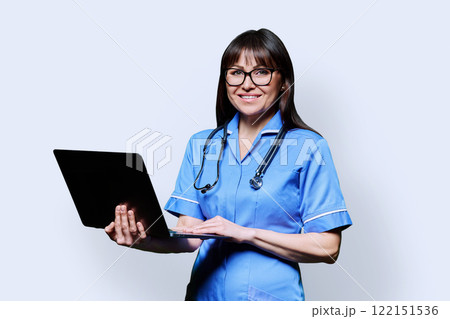 Female nurse holding laptop, looking at camera on white studio background Female nurse holding laptop, looking at camera on white studio background 122151536