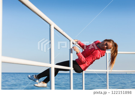 Woman fool around sitting on handrail near sea Woman fool around sitting on handrail near sea 122151898