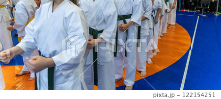 A close-up of a row of young athletes in white karate kimonos with clenched fists. 122154251