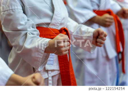 A close-up of a row of young athletes in white karate kimonos with clenched fists. 122154254