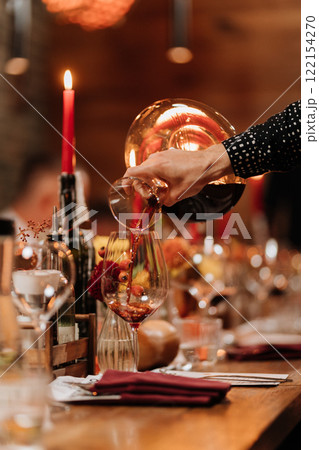 Decanting red wine into a glass on a festive dinner table with elegant decor and candlelight Decanting red wine into a glass on a festive dinner table with elegant decor and candlelight 122154270