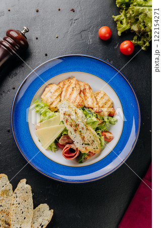 Grilled chicken salad with cheese slices, bacon, lettuce, and crispy bread for a hearty, fresh meal 122154271