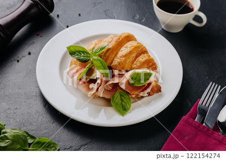 Fresh croissant sandwich with prosciutto and basil served on plate, perfect for a gourmet breakfast Fresh croissant sandwich with prosciutto and basil served on plate, perfect for a gourmet breakfast 122154274