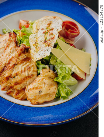 Grilled chicken salad with cheese slices, bacon, lettuce, and crispy bread for a hearty, fresh meal 122154279