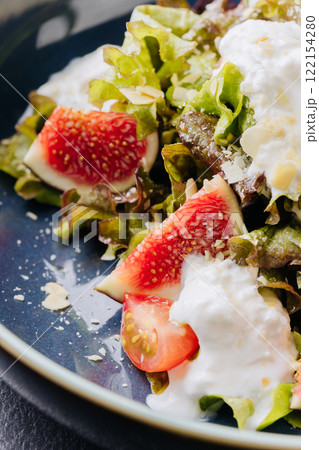 Fresh fig and burrata salad with leafy greens, almonds, and creamy dressing in a rustic blue bowl 122154280