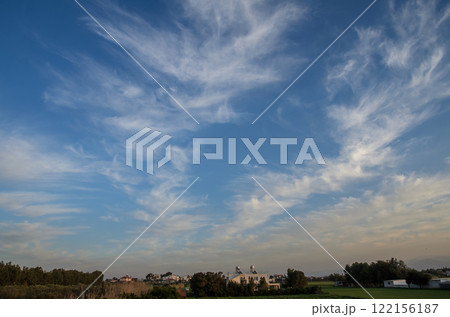 Breathtaking wispy clouds stretch across a vibrant sky near a serene countryside landscape 122156187