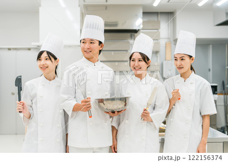 厨房・キッチンに立つコックコート姿の調理師・シェフ・コックの男女 122156374