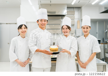 厨房・キッチンに立つコックコート姿の調理師・シェフ・コックの男女 122156622