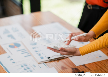 Close-up of hands using a calculator with financial charts on a desk, highlighting business analysis and financial planning. 122156663