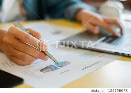 Close-up of hands working on financial charts and laptop, illustrating business analysis and productivity. Close-up of hands working on financial charts and laptop, illustrating business analysis and productivity. 122156678