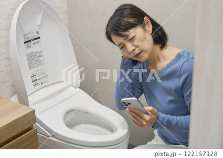 トイレでスマホでを持って困っている女性 122157128