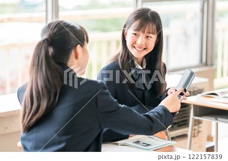 学校の教室でスマホを見ながら会話する中学生の女子生徒 122157839