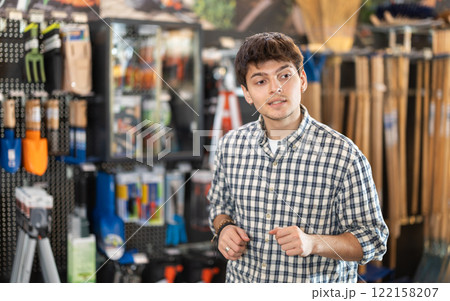 In hardware store department, young man looking for something on shelf of showcase 122158207