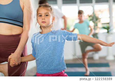 Girl and boy with her mother and dad doing exercises in pair during family workout in modern yoga studio 122158389