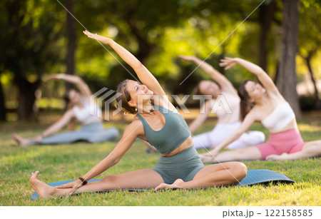 Girls practicing hatha yoga in summer garden, stretching in an asymmetrical seated asana Parivritta Janu Sirsasana with  122158585