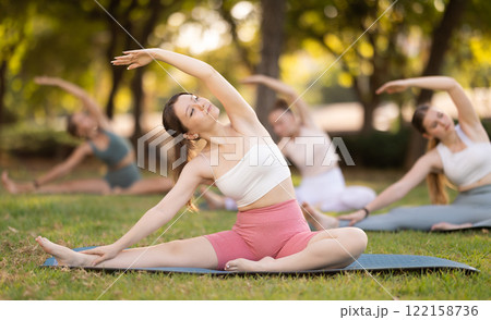 Girls practicing hatha yoga in summer garden, stretching in an asymmetrical seated asana Parivritta Janu Sirsasana with a forward bend and an outstretched arm 122158736