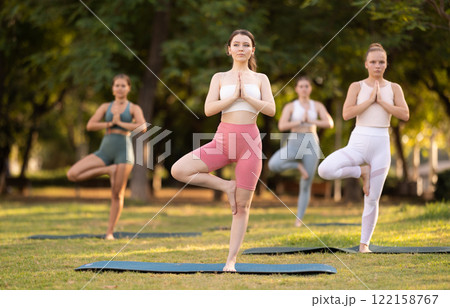 Group of young women doing yoga in tree pose 122158767