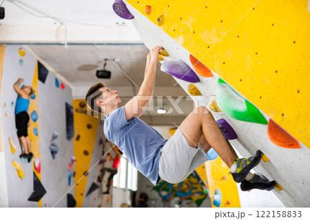 Young man climbing on rock-climbing wall Young man climbing on rock-climbing wall 122158833