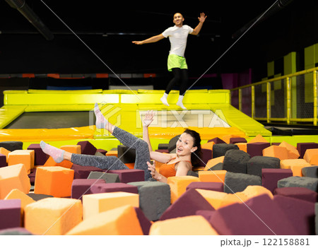 Fitness, fun, leisure and sport activity concept - happy woman fell on soft, safe filler cubes after jumping on trampoline Fitness, fun, leisure and sport activity concept - happy woman fell on soft, safe filler cubes after jumping on trampoline 122158881
