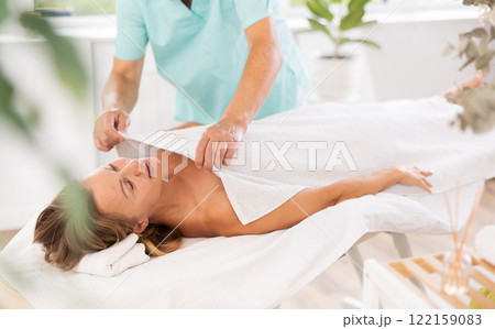 Relaxed middle-aged woman lying on massage table covered with blanket by masseuse 122159083