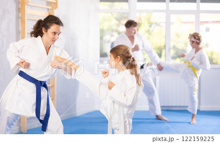 Preteen girl in kimono practicing karate kicks during sparring with mother Preteen girl in kimono practicing karate kicks during sparring with mother 122159225