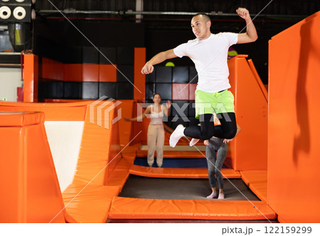 Joyful young man jumping on trampolines in colorful amusement park 122159299
