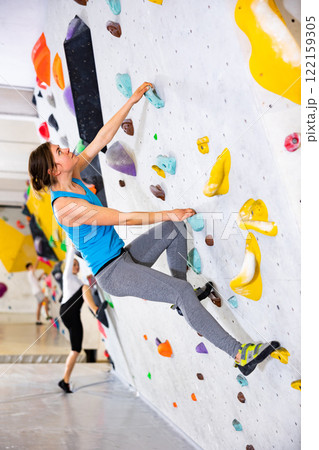 Young cheerful positive sporty woman training at bouldering gym without special climbing equipment 122159305