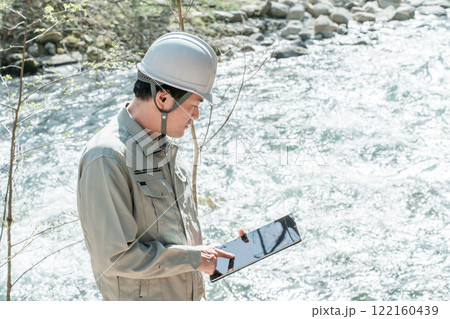 川・河川で河川調査・水質調査をする作業服姿の施工管理技士の男性 122160439