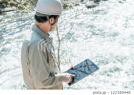 川・河川で河川調査・水質調査をする作業服姿の施工管理技士の男性 122160440