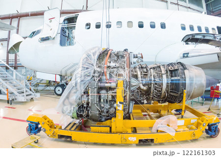 Close-up of high-bypass turbofan aircraft engine near to a passenger aircraft in a hangar 122161303