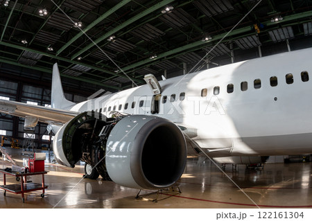 White passenger airliner in the aviation hangar. Aircraft under maintenance. Checking mechanical systems for flight operations White passenger airliner in the aviation hangar. Aircraft under maintenance. Checking mechanical systems for flight operations 122161304