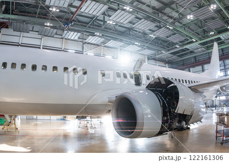 White passenger airliner in the aviation hangar. Jetliner under maintenance. Checking mechanical systems for flight operations 122161306