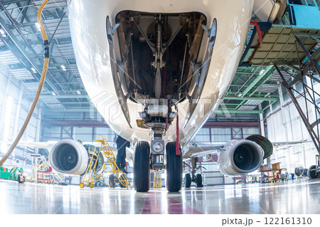 White passenger airliner in the hangar. Bottom view of the jet plane under maintenance. Checking mechanical systems for flight operations White passenger airliner in the hangar. Bottom view of the jet plane under maintenance. Checking mechanical systems for flight operations 122161310